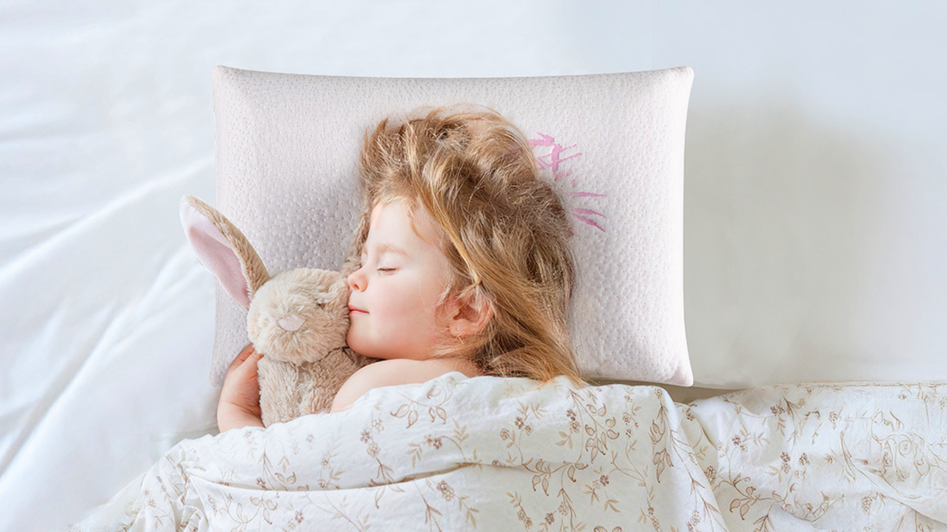 Little girl sleeping soundly with a teddy bear on a Attababy toddler pillow
